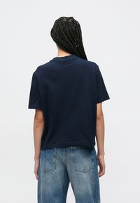 Μπλε σκούρο βαμβακερό t-shirt με κοντά μανίκια, άνετη εφαρμογή και στρογγυλή λαιμόκοψη. Συνδυασμένο με ανοιχτό μπλε, ψηλόμεσο τζιν παντελόνι.