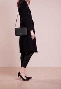 Černý kabát s dlouhým silueta, spárovaný s černými koženými legínami a černými špičatými podpatky. Malá  černá taška s řetízkovým popruhem.