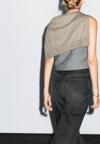 Grauer Cropped-Top mit einem Overlay in einem hellbraunen Farbton, kombiniert mit hoch geschnittenen schwarzen Jeans, die über hintere Taschen und eine klassische Silhouette verfügen.