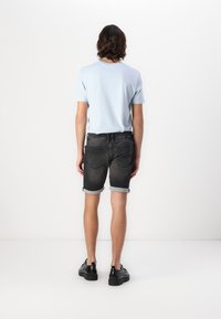 T-shirt en coton bleu à manches courtes, associé à un short en denim foncé avec des revers roulés. Des chaussures noires complètent la tenue.