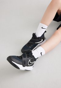 Černé a námořnické sportovní boty s texturovaným svrškem a bílými akcenty, které mají suchý zip a jsou spárovány s bílými ponožkami Nike.