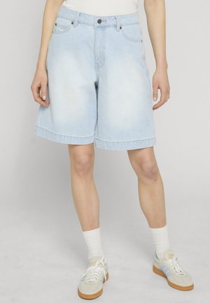 Osoba nosiaca svetlomodré rifľové šortky po kolená, biele ponožky a biele tenisky s svetlomodrými pruhmi.