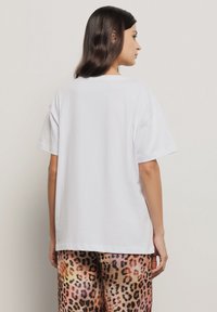 T-shirt bianco in cotone con maniche corte, dalla vestibilità comoda e colletto a girocollo. Indossato con pantaloni stampati con motivo leopardato multicolore.