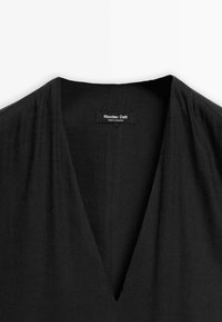 Musta V-kaula-aukko mekko, jossa on rento siluetti, sileä tekstuuri ja etiketti, jossa lukee "Massimo Dutti", valmistettu Marokossa.