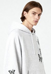 Felpa con cappuccio grigia con finitura testurizzata, caratterizzata da un ricamo nero a farfalla sul davanti e sulla manica. Cappuccio regolabile con coulisse.