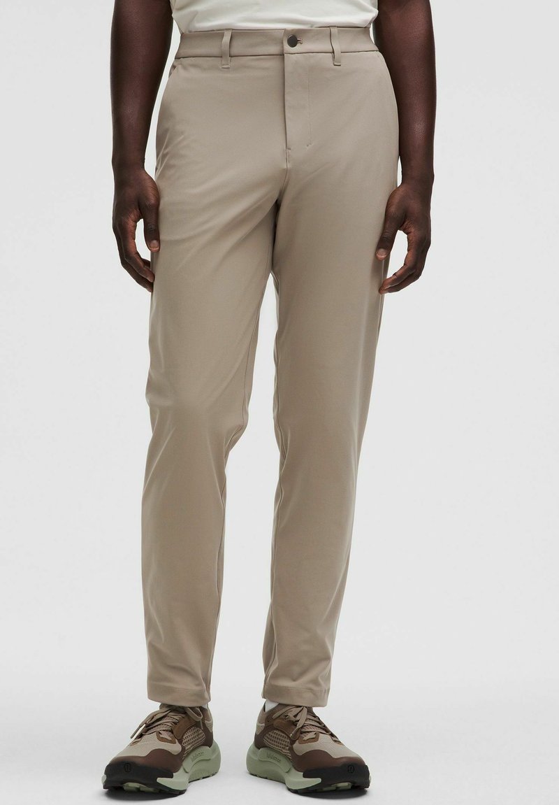 Bež rastezljive hlače uskog kroja, s prednjim kopčanjem na dugme i dva bočna džepa. U kombinaciji sa smeškim i zelenim patikama.