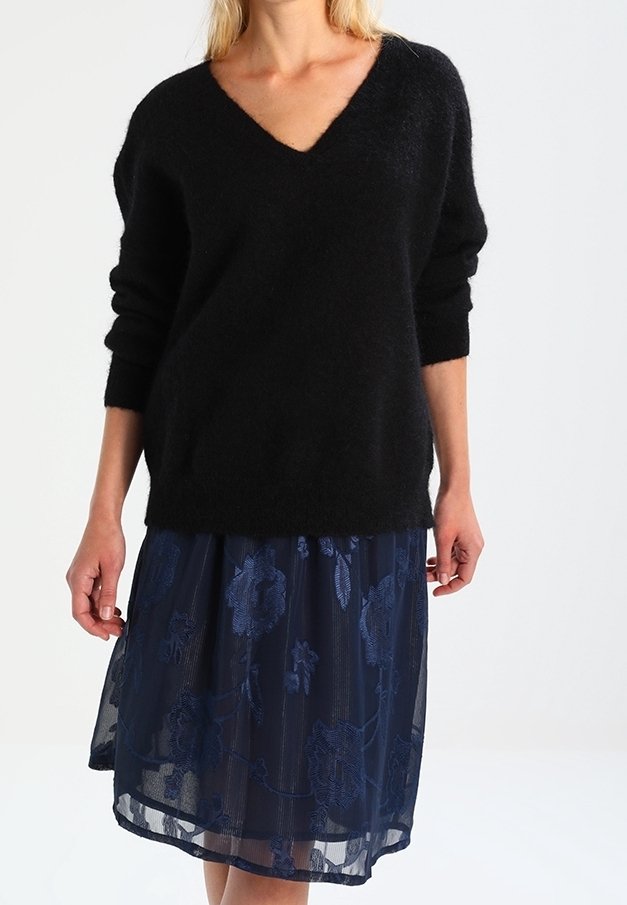 Schwarzer, flauschiger V-Ausschnitt-Pullover kombiniert mit einem dunkelblauen, durchsichtigen Rock mit floralen Stickereien. Lange Ärmel und lässige Passform.