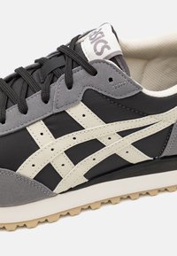 Black and grey athletic shoe featuring suede and fabric materials, with cream accents and signature branding on the tongue.