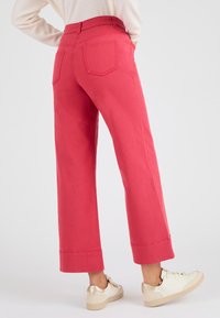 Pantalones de pierna ancha rosa con dobladillos, que presentan una textura suave y dos bolsillos traseros. Combinados con zapatillas blancas y doradas.