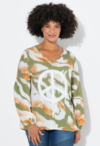 Blusa a maniche lunghe verde e bianca con un grande simbolo della pace. Pattern astratti arancioni e bianchi decorano il tessuto, con un design a scollo a V.