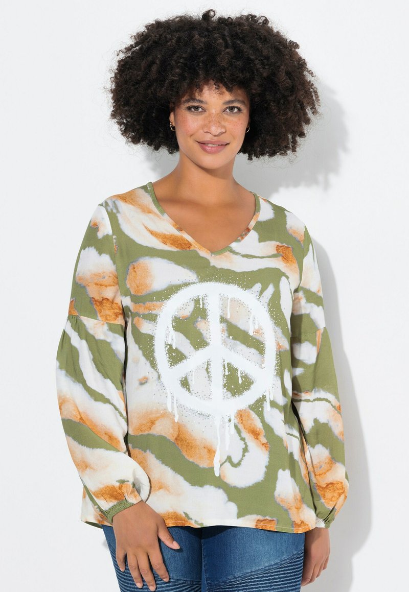 Blusa a maniche lunghe verde e bianca con un grande simbolo della pace. Pattern astratti arancioni e bianchi decorano il tessuto, con un design a scollo a V.