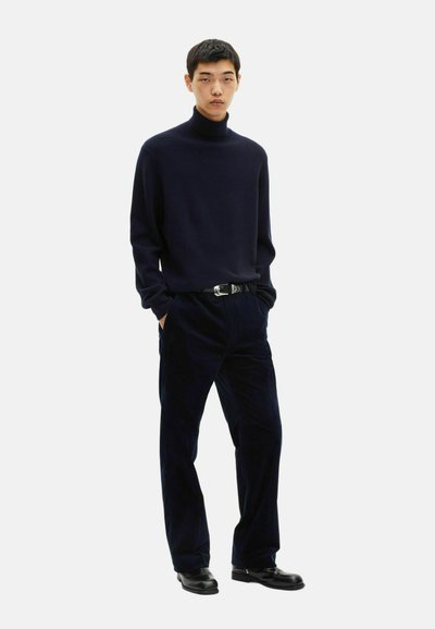 Navyblauer Rollkragenpullover aus weichem Strick, kombiniert mit weit geschnittenen, navyblauen Cordhosen. Ein schwarzer Gürtel und polierte schwarze Schuhe runden das Ensemble ab.