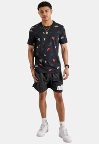 T-shirt nera Nike con stampe di logo colorate, abbinata a pantaloni corti neri con un bold logo bianco e sneakers bianche con dettagli neri.