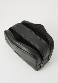 Black leather toiletry bag with a rectangular shape, featuring two zippered compartments and textured surface. Silver-tone hardware accents.