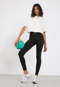 Colanți negri cu talie înaltă asortați cu un tricou alb scurt. Ținând o minge turcoaz, purtând încălțăminte sport argintie cu accente negre.