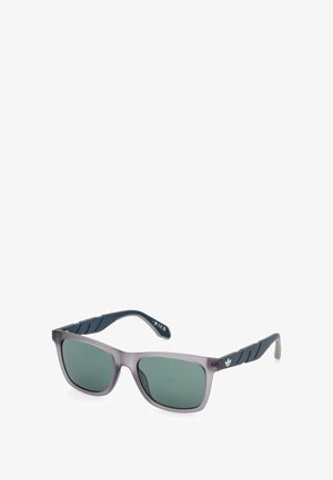 Gafas de sol con un marco gris mate y lentes verdes oscuros. Las varillas presentan un material texturizado en color azul marino con un sutil detalle del logo.