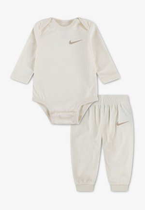 Babydragt i flødefarvet med lange ærmer og matchende bukser med elastisk talje, begge med en lille brun Nike swoosh-logo.