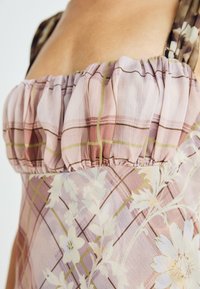 Top rosa e stampato con scollo arricciato, caratterizzato da disegni floreali e linee a quadretti in tonalità chiare, realizzato in un tessuto morbido e leggero.