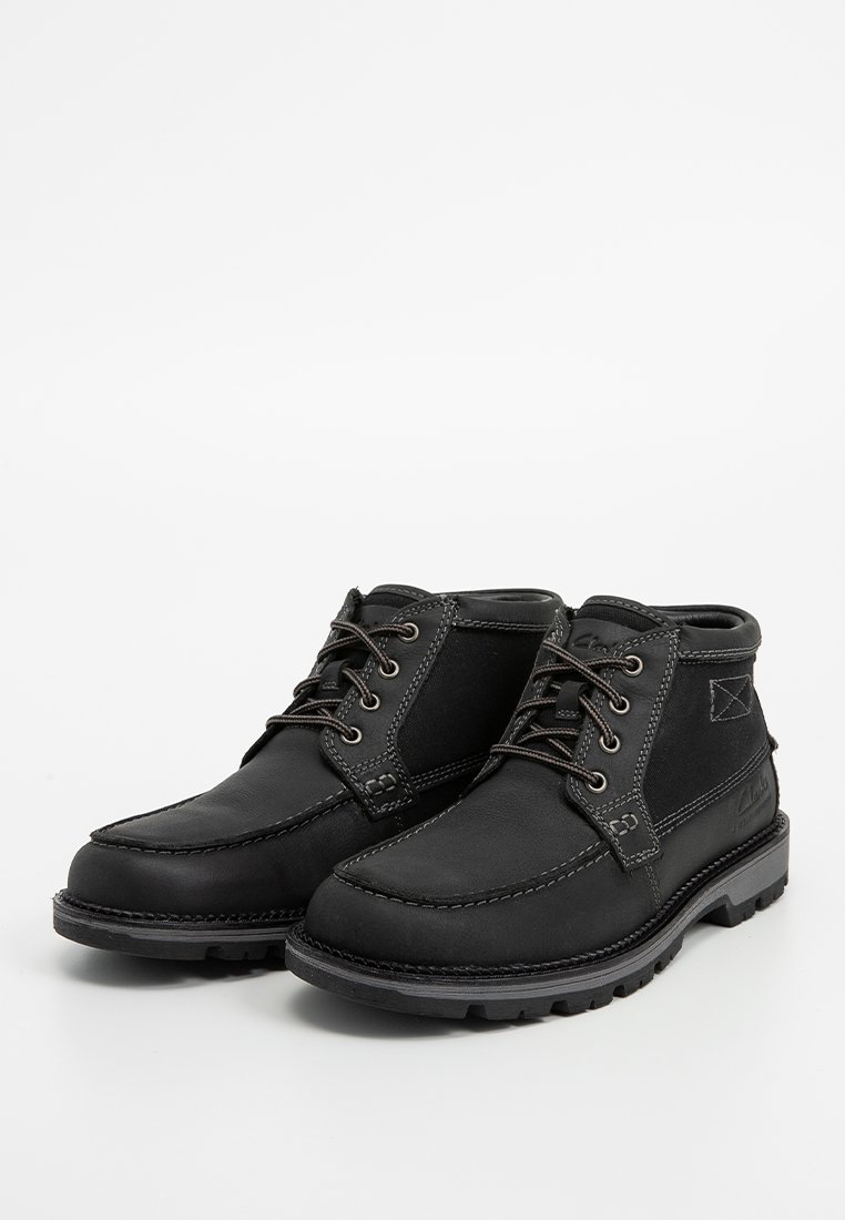 Botas negras de cuero y lona, con cierre de cordones, puntera redonda, suela robusta y detalles de costura en contraste.