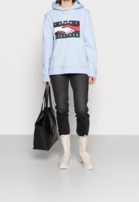 Jasnoniebieska bluza z kapturem z grafiką, ciemne dżinsy, beżowe botki za kostkę i czarna torba na ramię. Miękka tkanina, luźny krój i wbudowany sznurek.