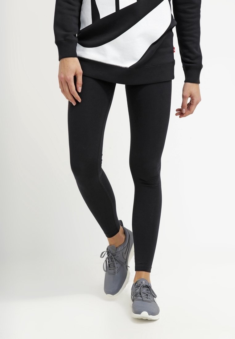 Svarta leggings i elastiskt material, kombinerat med en lös svart och vit grafisk sweatshirt samt grå sportskor.