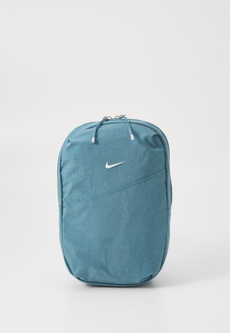 Tirkizna Nike naprtnjača s glatkom teksturom, zakrivljenim dizajnom i srebrnim logom. Ima dvostruke patentne zatvarače i dijagonalne šavove.