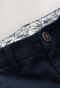 Tengerészkék nadrág sima textúrával, barna gombbal és fehér belső béléssel, amely kék leveles mintázattal díszített.