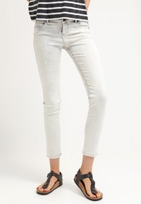 Jeans ajustados de lavado claro con una textura desgastada, combinados con sandalias planas negras con suela de corcho y tiras anchas.