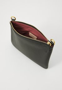 Borsa a busta in pelle nera con superficie texturizzata, zip dorata e foderatura bordeaux. Presenta un'etichetta interna e un dettaglio con manico rotondo.
