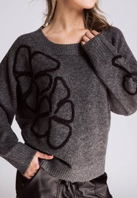 Grauer Wollpullover mit großem schwarzem Blumenstickerei, gerippten Bündchen und Saum. Lockerer Schnitt mit weitem Ausschnitt und strukturierter Oberfläche.