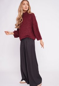 Maroon textured sweater with loose fit and ribbed neckline, paired with black wide-leg trousers and white sneakers.