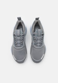 Ett par gråa sportskor med meshöverdelar, reflexdetaljer på tårna och märkta etiketter på snören och hälöglor, visade ovanifrån.