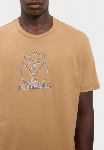 T-shirt en coton beige avec un graphique d'ours et le texte brodé "ICEMBARG" en dessous. Manches courtes et col rond classique.
