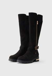 Knielange schwarze Wildlederstiefel mit einem Reißverschluss an der Seite, goldfarbenen Akzenten, einer flexiblen Gummisohle und einem breiten Bund für zusätzlichen Komfort.