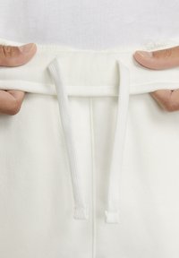 White sweatpants featuring a drawstring waistband, with a soft, textured fabric and reinforced stitching at the seams.