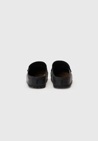 Chaussures noires à enfiler avec un bout arrondi et un dos bas, dotées d'une semelle en caoutchouc texturé et d'un dessus en simili cuir lisse.