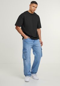 Sort oversized bomulds T-shirt, lyseblå cargo jeans med sidelommer og hvide sneakers. Enkel, afslappet pasform, glat tekstur.