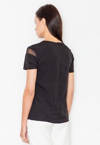 Czarny krótki top z krótkim rękawem z przeźroczystymi siateczkowymi akcentami na ramionach, okrągłym dekoltem oraz zapięciem na zamek z tyłu. Gładka tkanina o usztywnionym kroju.