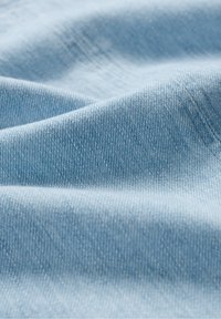 Jasnoniebieska tkanina denimowa o gładkiej fakturze z subtelnym wzorem tkaniny oraz delikatnym wyblaknięciem w niektórych obszarach, podkreślająca miękkość i elastyczność.