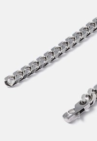 Pulseira de corrente de metal prata com elos entrelaçados e acabamento polido. Inclui um fecho com detalhe do nome da marcagravado.