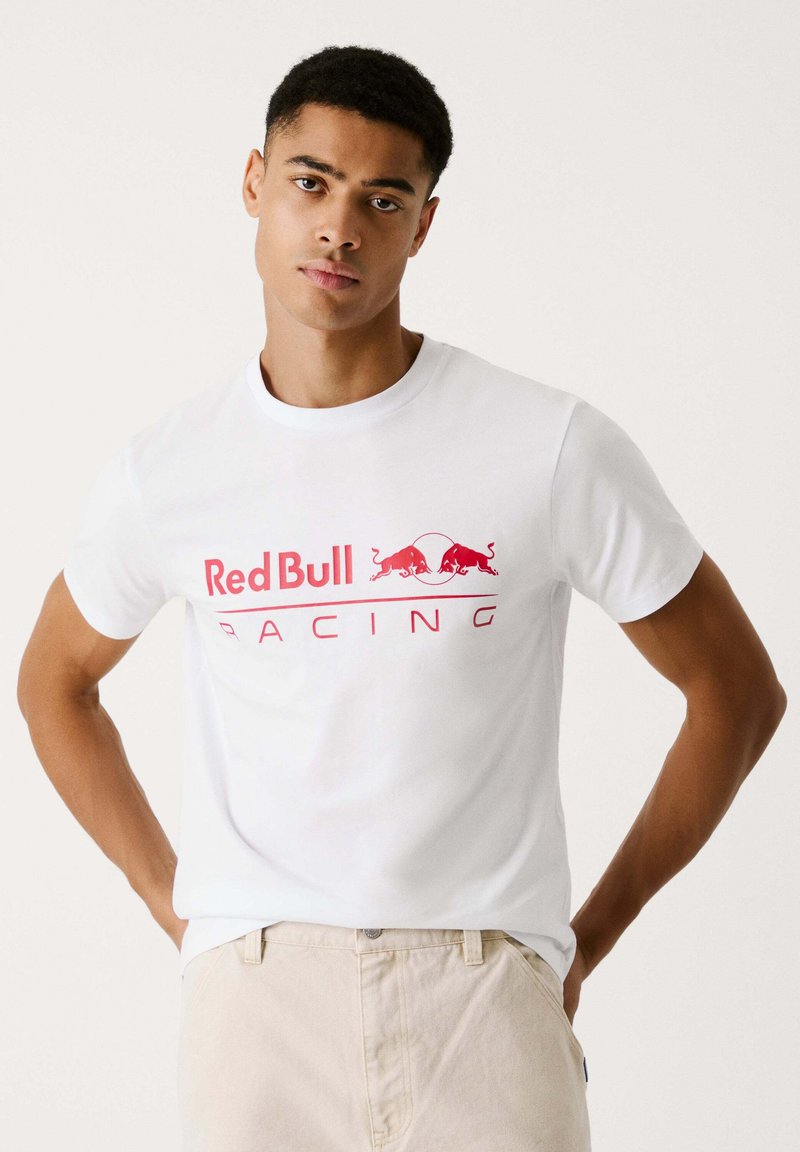 Witte T-shirt met korte mouwen, voorzien van een opvallend rood 'Red Bull Racing' logo en twee rode stierenafbeeldingen in het midden. Gedetailleerd met een ronde hals.