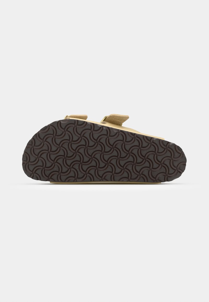 Schuhe mit einem beigen Obermaterial, zwei verstellbaren Riemen und einer strukturierten, dunkelbraunen Gummisohle mit einem wirbelnden Muster.