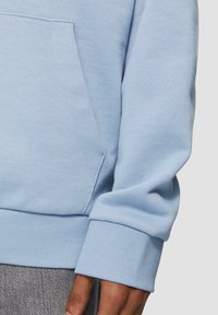 Lichtblauwe sweatshirt met een geribde onderrand en manchetten, voorzien van een kangoeroezak en een gladde textuur. De stof lijkt zacht en van fleece-voering te zijn.