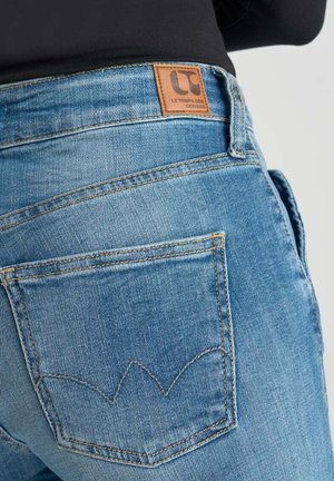 Blue denim jeans with a textured finish, featuring a leather brand patch and distinctive stitching on the back pockets.