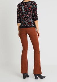 Suéter negro con estampado floral, de mangas largas, combinado con pantalones acampanados ceñidos de color óxido y botines negros de tacón.