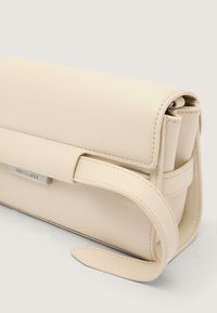 Beiger Lederhandtasche mit strukturiertem Design, ausgestattet mit einer klappbaren Klappe, gesteppten Akzenten und einem silbernen Markenlogo.