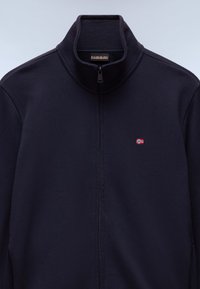 Marineblå zipper-jakke med høj krave, der har et lille broderet Norges flag. Lavet af blødt materiale med en glat tekstur og uden synlige mønstre.