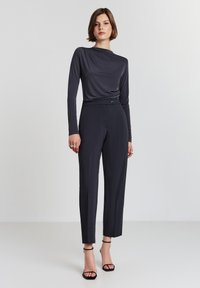 Top a maniche lunghe grigio scuro con design drappeggiato, abbinato a pantaloni dritti e strutturati. Tacchi neri con cinturini completano l'outfit.