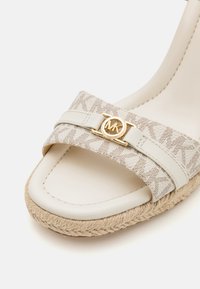 Beige espadrille sandal with a woven jute sole, featuring a signature MK logo on a patterned fabric strap and a smooth leather band.