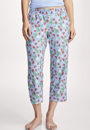 Woman wearing cropped light blue pajama pants with red strawberry and green leaf pattern standing barefoot